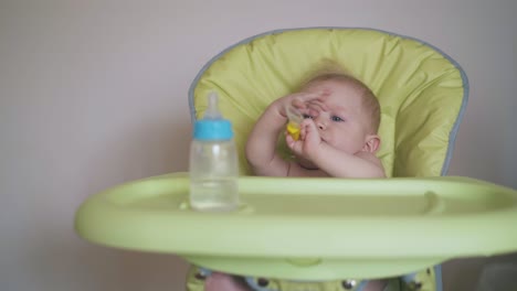 mother-gives-spoon-to-little-son-sitting-in-green-highchair