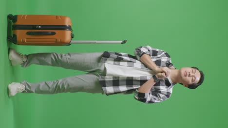 full body of asian male traveler with luggage praying for something while standing in the green screen background studio