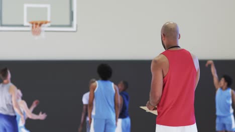 diverse male basketball coach watching team training game at indoor court, in slow motion