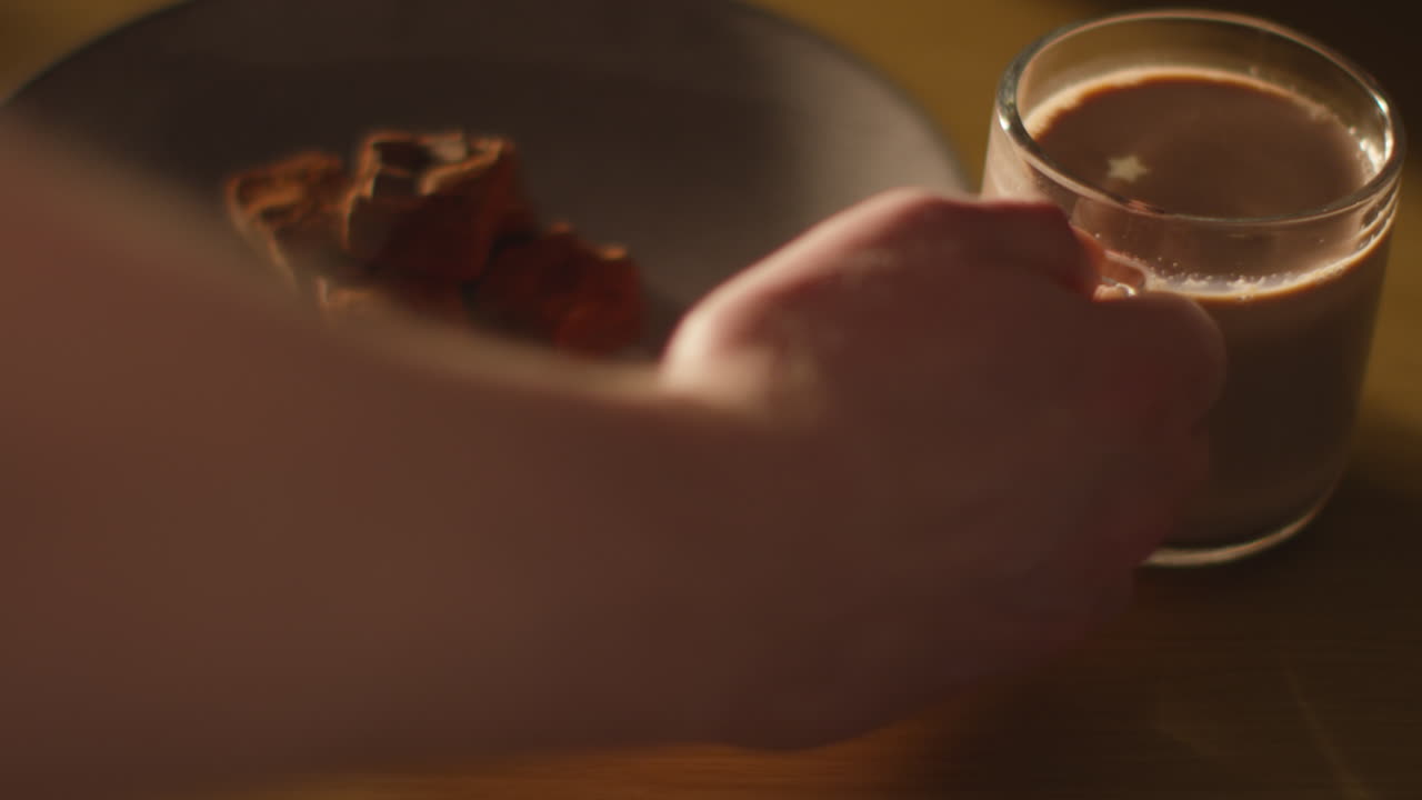 1개의 브라우니의 접시 에 있는 테이블 위에 뜨거운 초콜릿 음료의 증기 컵을 집어 들고 있는 사람의 근접 사진