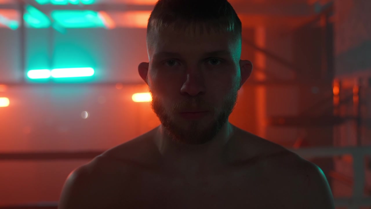Intenso combattente uomo che fissa la telecamera in un ring illuminato al neon