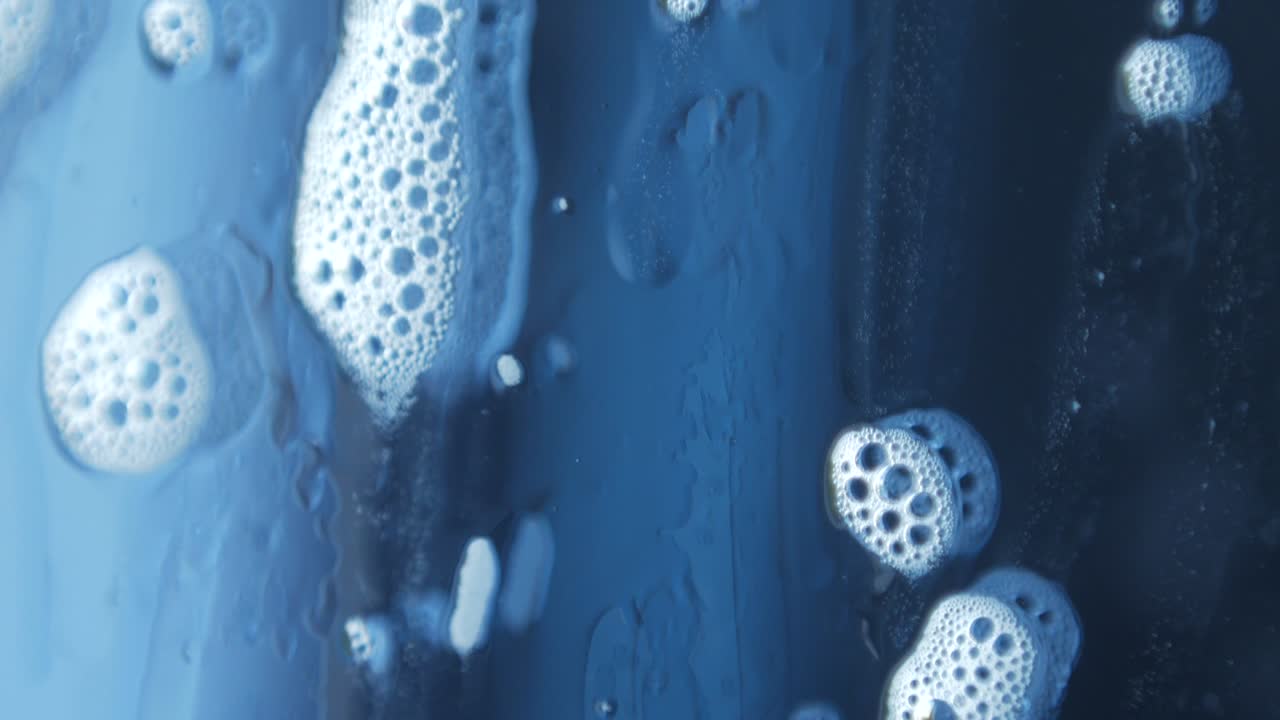 비누 거품의 매크로 사진, 창문 청소 화학, 유리 아래로 흐르는 아름다운 반사.