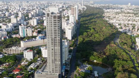 Vista-Aérea-Escénica-Del-Alto-Rascacielos-Residencial-De-La-Avenida-Anacaona-Y-El-Centro-De-La-Ciudad-De-Santo-Domingo-Y-Vista-Del-Agua-Del-Mar,-República-Dominicana,-Descenso-De-Drones-Aéreos