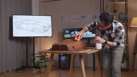 asian man automotive designer spraying and using sponge to smooth out the surface of the sculpture of car clay in the studio