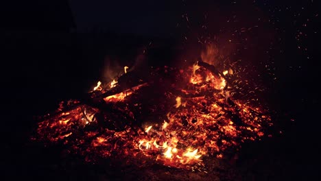 red flashing and smoldering coals of a fire. sparks from the fire at night. a man turns over firewood with a pitchfork