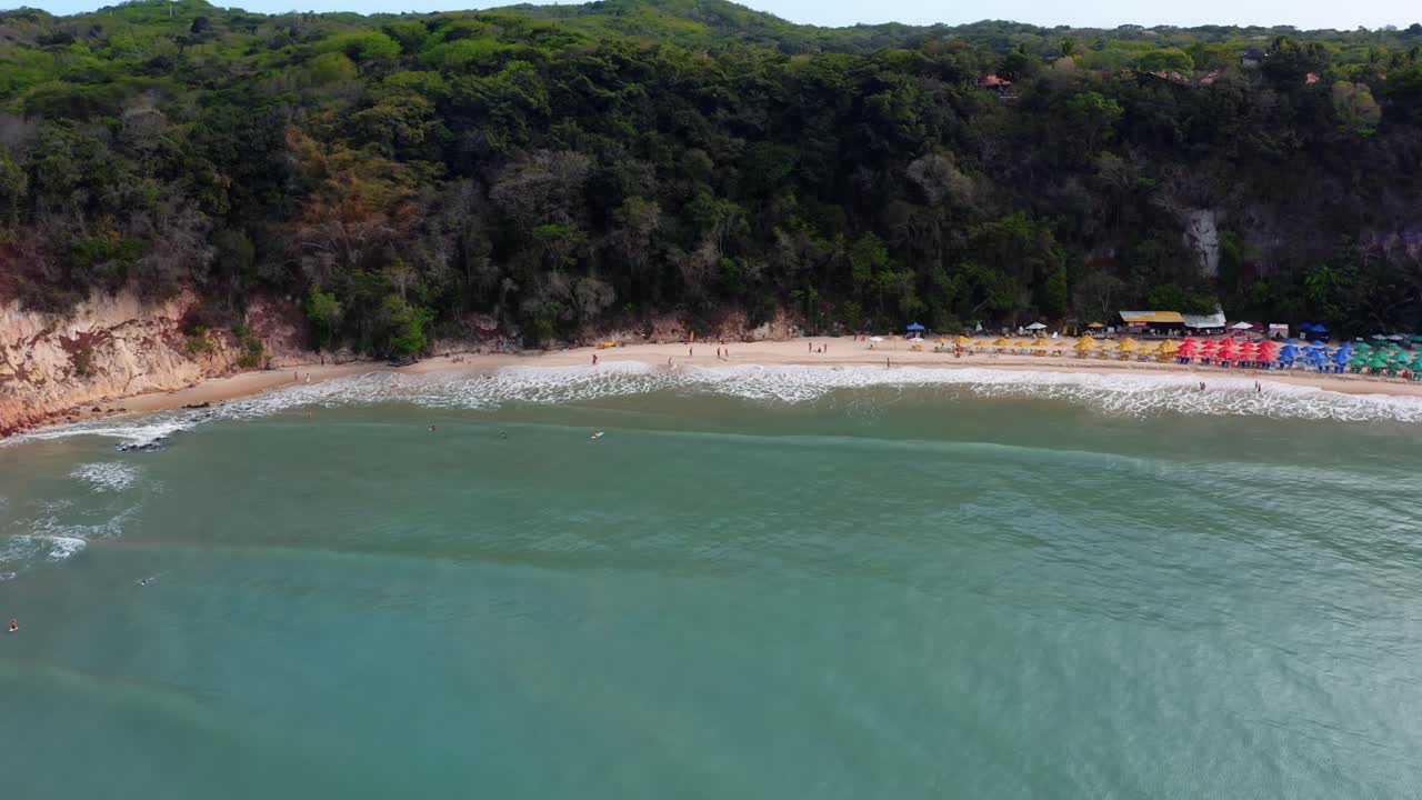 magnífica plataforma de drones aéreos en una toma de la playa tropical praia do madeiro con coloridas sombrillas y turistas nadando y surfeando cerca de la famosa ciudad de pipa en el norte de brasil