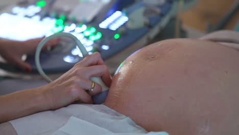 ultrasonic diagnostics for a pregnant lady. big round abdomen being checked by the device in doctor's hand. close up.