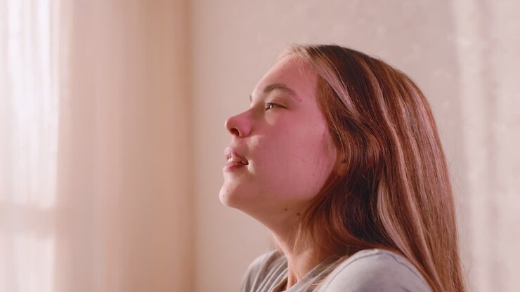 Close up side view of elegant lady with eyes closed gently rolling shoulders after peaceful sleep, soft natural morning light streaming through curtain illuminating relaxed face