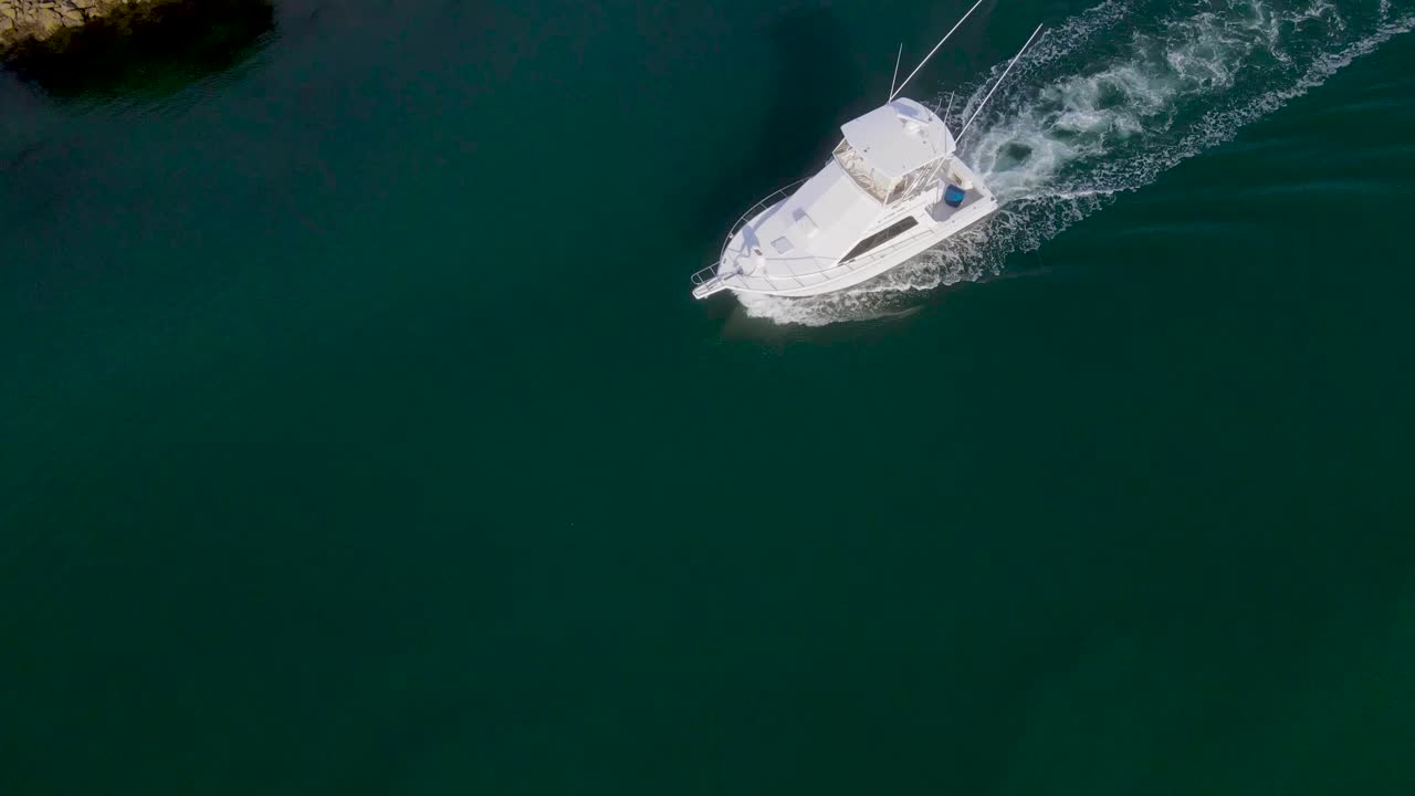 Panoramica aerea verso l'alto su un peschereccio che rientra in porto nell'oceano aperto.
