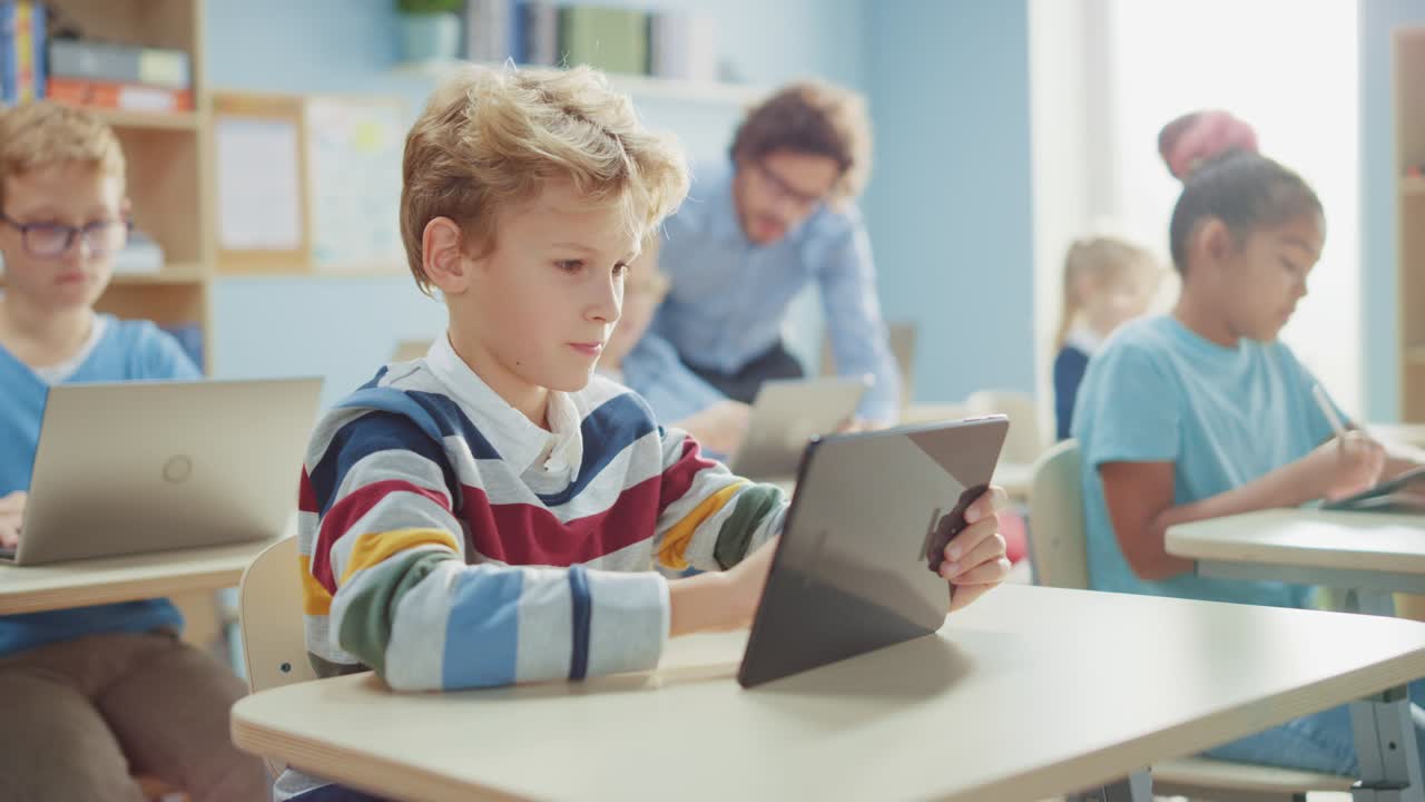 clase de ciencias de la computación de la escuela primaria: un niño lindo usa una tableta digital, sus compañeros de clase también trabajan con portátiles. niños que reciben educación moderna en el tallo, jugando y aprendiendo