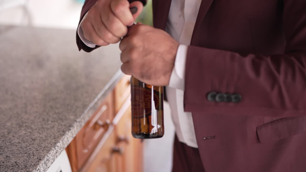 Close up of a man in a burgundy suit opening a bottle on a granite countertop indoors