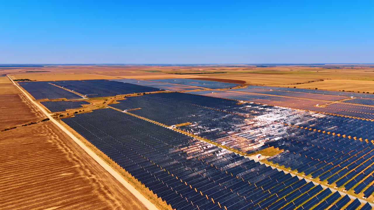Expansive solar farm in sunny landscape. Rows of solar panels stretch across the landscape under a bright blue sky, generating renewable energy efficiently