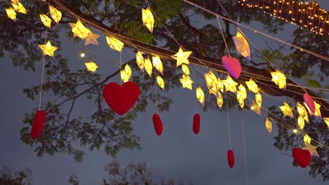 red hearts hanging on a tree with many paper stars and lights twinkling at night. valentine's day concept