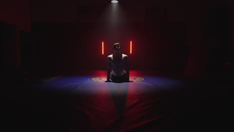 boxeador de kickbox estirándose antes del entrenamiento de mma, atleta masculino, estudio de gimnasia oscuro