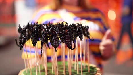 person holding tray of edible scorpions on sticks in thailand