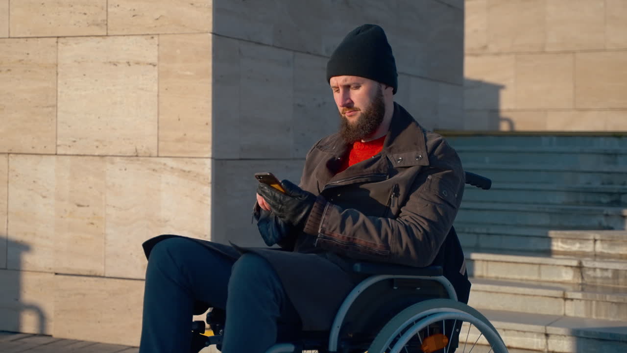 hombre en silla de ruedas usando un teléfono inteligente al aire libre