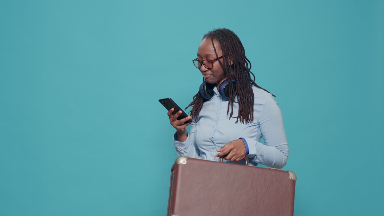 African american woman carrying suitcase trolley and texting messages