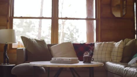 Acogedor-Interior-De-Cabina-Con-Café-Humeante-Y-Libros-Sobre-Una-Mesa-Junto-A-Una-Ventana