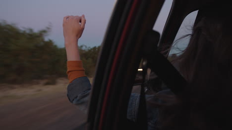 Mujer-En-El-Coche-Sosteniendo-La-Mano-Por-La-Ventana-Sintiendo-El-Viento-Soplando-Entre-Los-Dedos-Conduciendo-En-El-Campo-En-Un-Viaje-Por-Carretera-Viajando-Para-Vacaciones-De-Verano-Disfrutando-De-La-Libertad-En-La-Carretera-Al-Amanecer