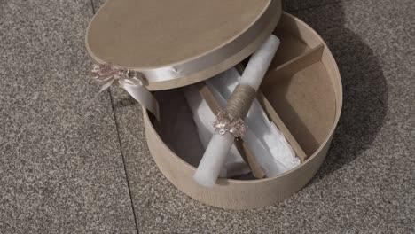caja redonda decorativa con una vela bautismal y una cinta en una superficie de piedra