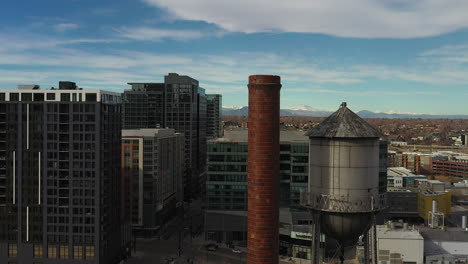 rising aerial drone footage of the meadow gold butter building and the water tower and chimney stack on top, in downtown denver, colorado