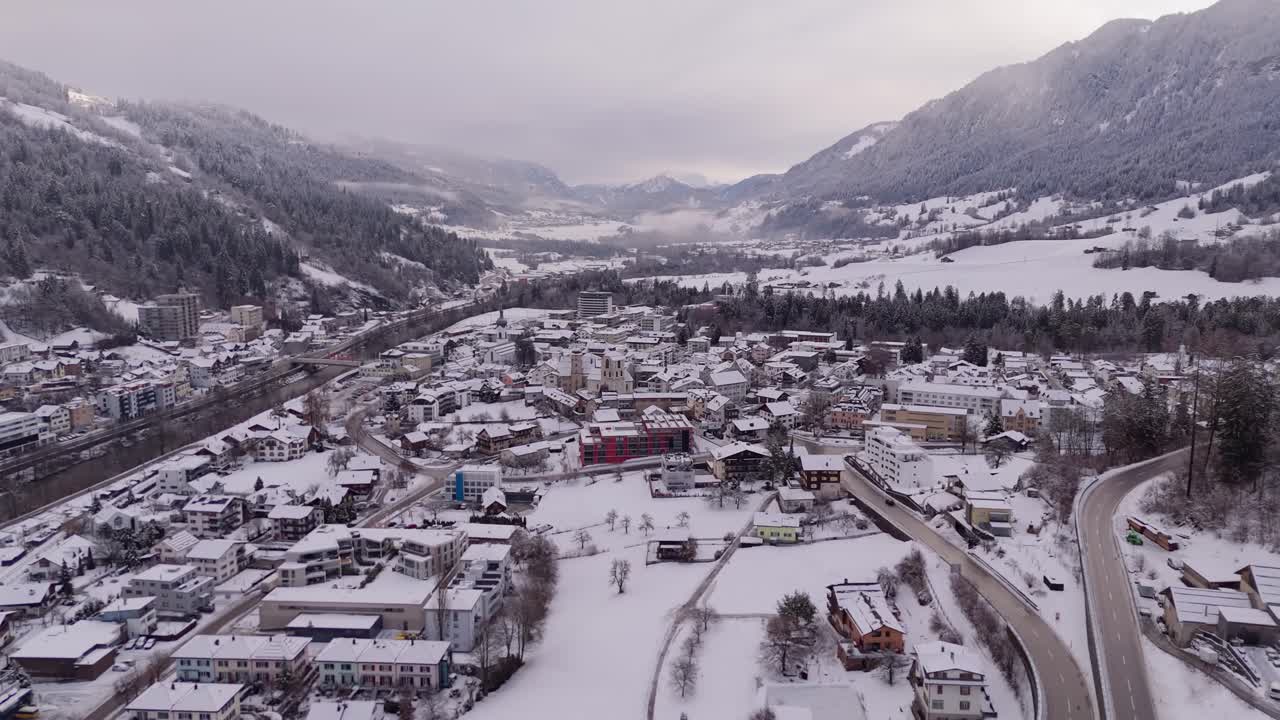White city of Illanz in Switzerland during grey cloudy winter day. Snow-covered roofs of houses and homes in small town. Aerial wide shot.