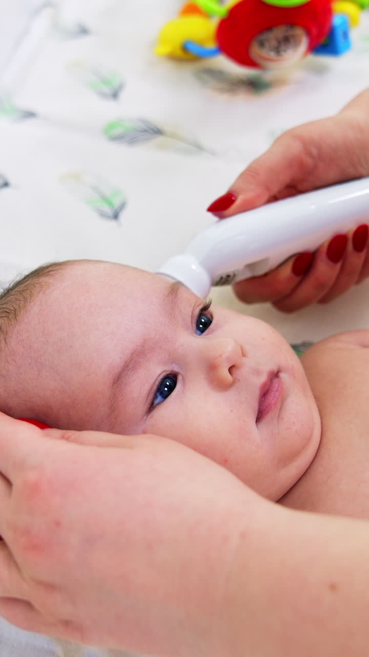 Caucasian infant boy lying on the doctor's table. Pediatrician takes baby's temperature with electric thermometer. Close up. Vertical video