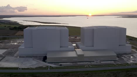 Nuclear-power-station-with-gorgeous-golden-sunset-by-a-river,-drone-high-angle