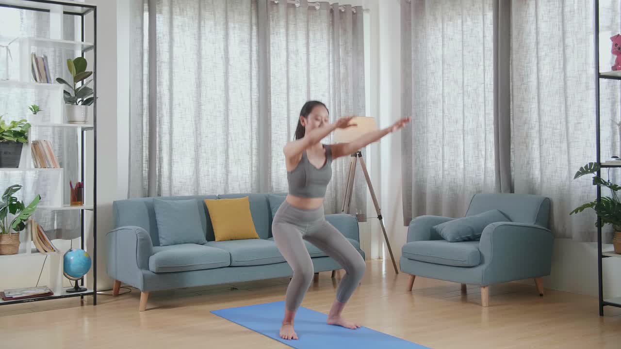 Young Asian Athletic Female In Sports Clothes Doing Butt Workout Squats On The Mat At Home