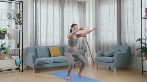 joven mujer atlética asiática en ropa deportiva haciendo sentadillas de entrenamiento de trasero en la alfombra en casa