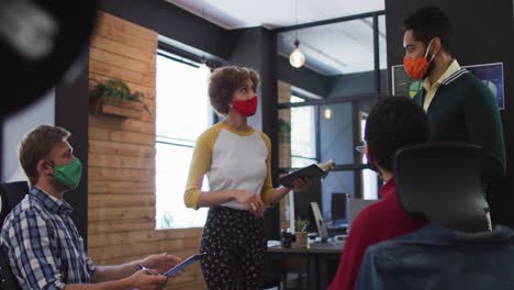 Diverse-colleagues-wearing-face-masks-discussing-together-at-modern-office