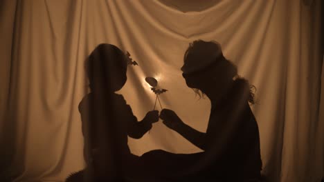 unrecognizable woman and boy telling spooky stories using shadow play and paper bats and pumpkins