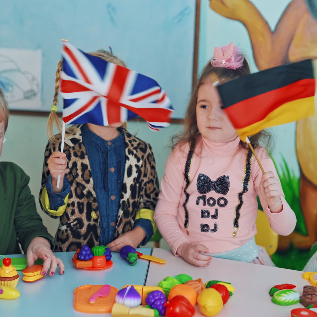 Little girls with English and German flags. Children in the classroom. Two curious girls holding flags and waving them on the background of educational center.