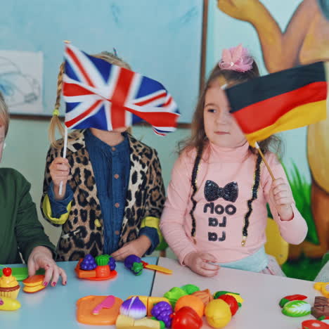 little girls with english and german flags. children in the classroom. two curious girls holding flags and waving them on the background of educational center.