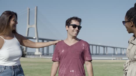 two female friends kissing handsome young man on meadow.