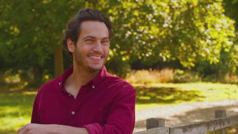 portrait of smiling casually dressed mature man leaning on fence on walk in countryside