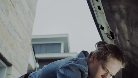 Woman-in-early-20s-checking-under-the-hood-of-a-truck-and-going-under-the-truck-to-find-and-fix-mechanical-problem