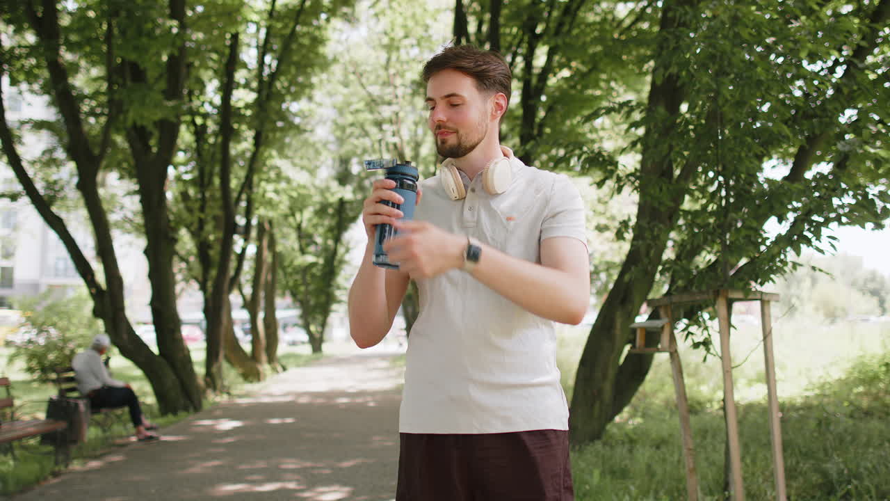 Sporty athletic thirsty man runner jogger drinking water after sport workout in park outdoors