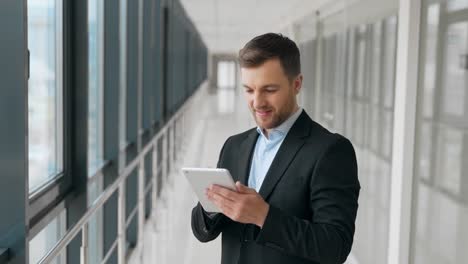 Happy-young-man-in-a-glass-corridor-spends-time-with-a-tablet