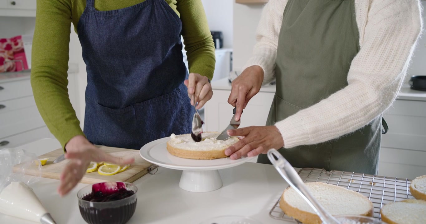 Confeiteiros no balcão colocando camada de bolo, fatiando limões, colocando geleia com colher e alisando o recheio para empilhar
