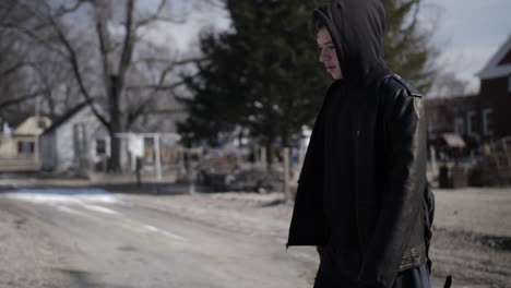 A-young-man,-high-school-aged-teenager-wearing-a-backpack-walks-down-a-road-during-the-winter-on-a-cold-day