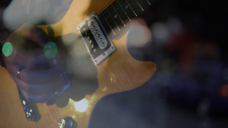 Elektro gitar yakın çekiminde elin girip tellere dokunarak akorları değiştirmesi, bokeh altında çalması