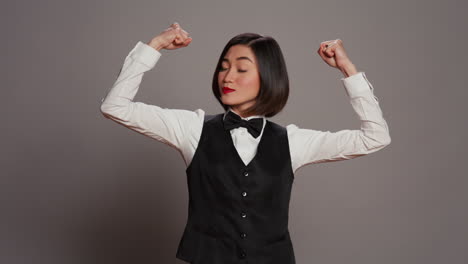 Asian-hotel-concierge-flexing-arms-muscles-in-grey-studio