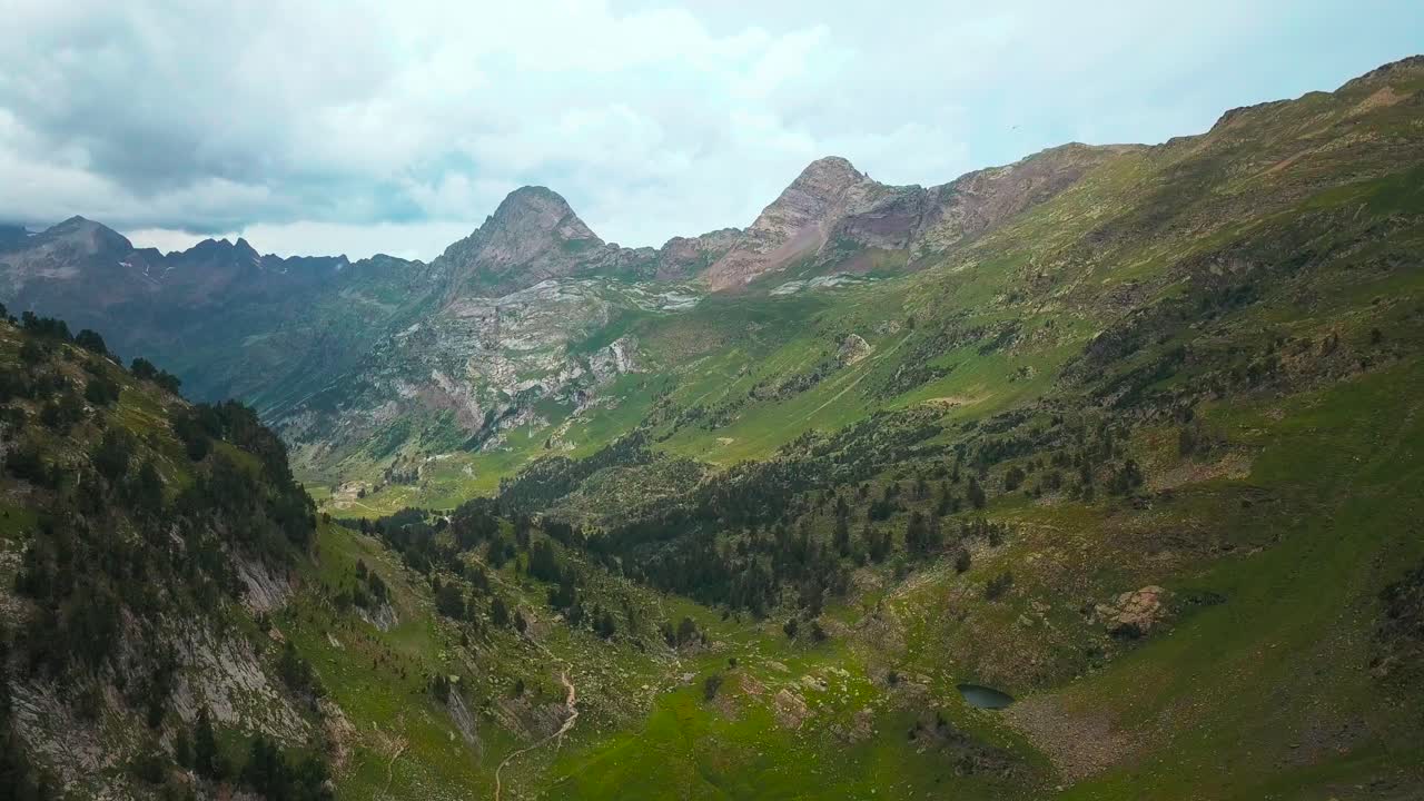 Rekaman udara horizontal 4K gunung-gunung besar di lingkungan alam hijau di Pegunungan Pirenia Spanyol.
