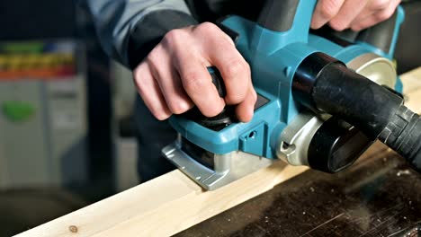 Close-up of a carpenter's hand working with an electric plane in a home workshop