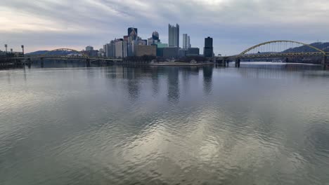 Deslizamiento-Aéreo-Sobre-El-Río-Ohio-Con-El-Horizonte-De-Pittsburgh,-El-Parque-Estatal-Point-Y-Los-Puentes-Amarillos-En-El-Fondo