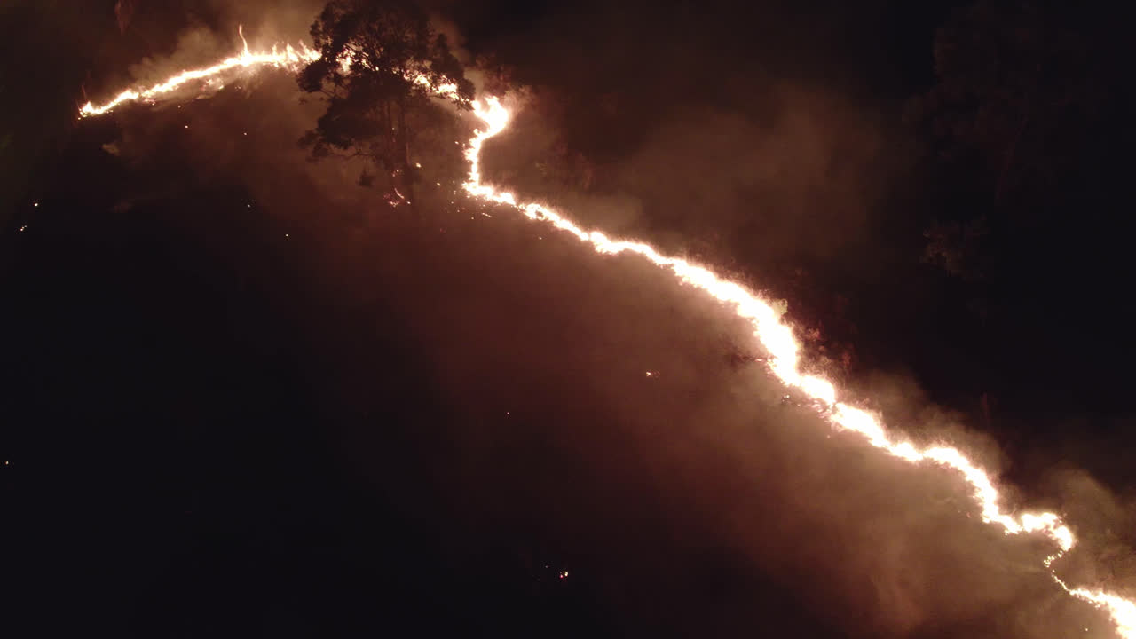 Aerial night view of fire spreading near a village with cars and people trying to combat the fire
