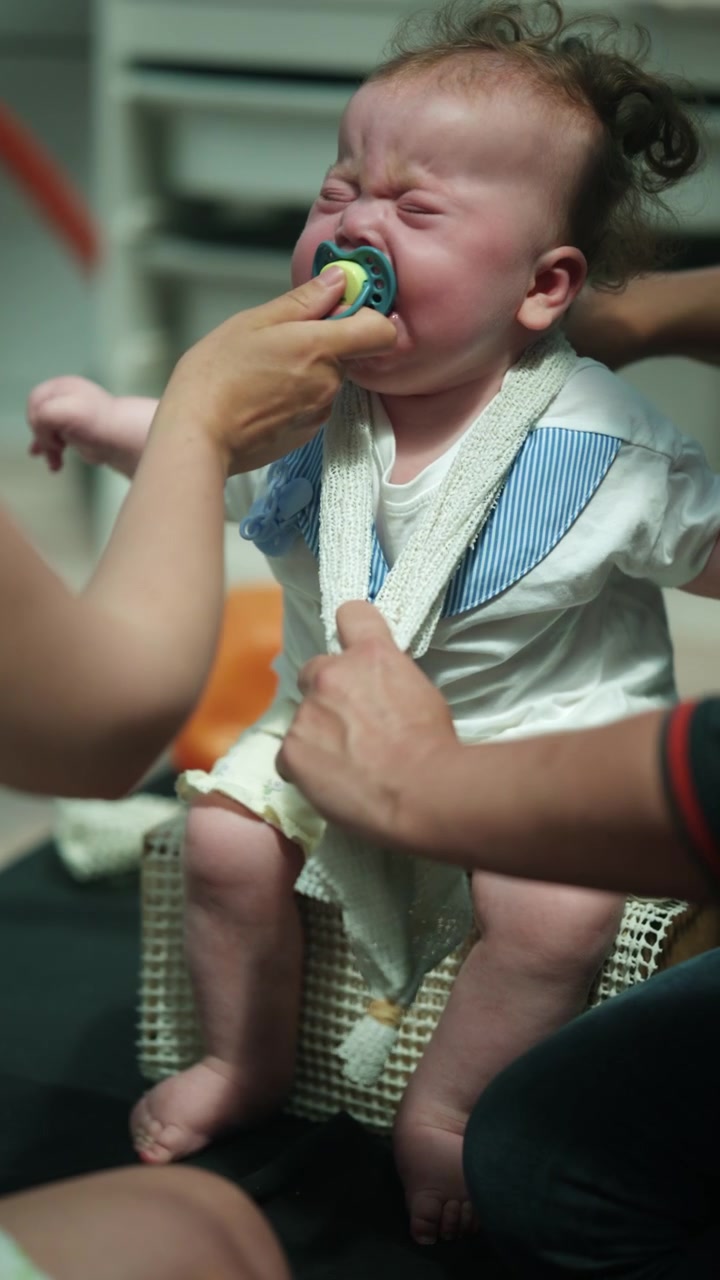 Parent hands trying to soothe upset infant with a pacifier during a diaper change, focusing on caregiving and emotional distress