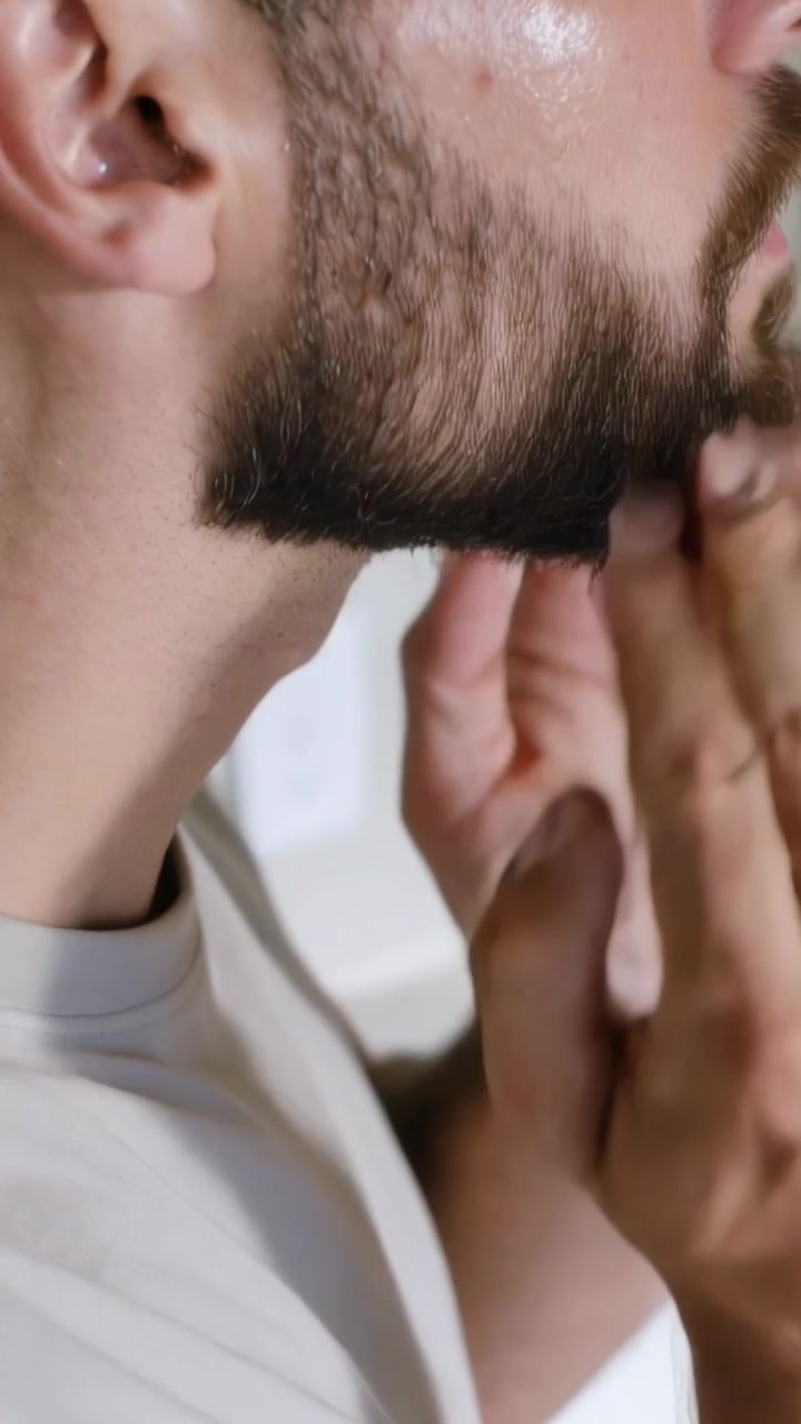 Video verticale: Uomo inclinato in avanti che si sistema la barba al lavandino dopo aver usato una bottiglia verde, con maglietta girocollo.