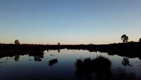 Low-angle-drone-shot-at-dusk-or-dawn-of-a-river-in-a-wetlands-landscape-located-in-peaceful-African-wilderness